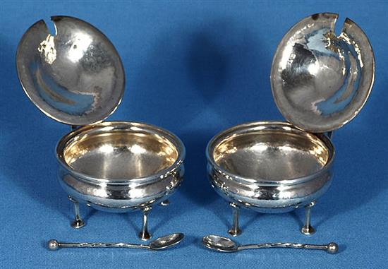 A pair of George V Arts & Crafts silver mustard pots with matching spoons, by Albert Edward Jones, width 90mm, weight 5.1oz/160grms.